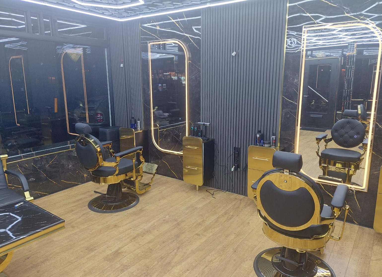 Het interieur van Mood Kapsalon: twee gouden kappersstoelen voor verlichte spiegels, zwart marmer en zwarte lamellenwanden.