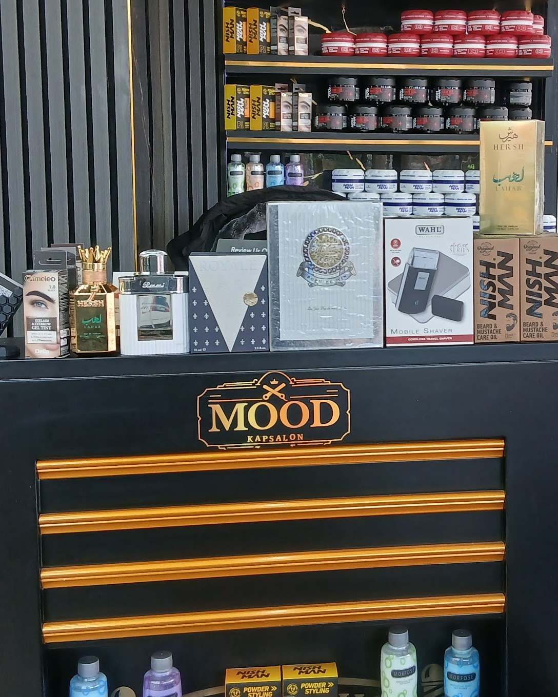 De toonbank van Mood Kapsalon met het gouden MOOD-bordje, gouden strepen en schappen vol haarproducten.